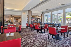 A restaurant with red chairs and tables, large windows, and a carpeted floor.