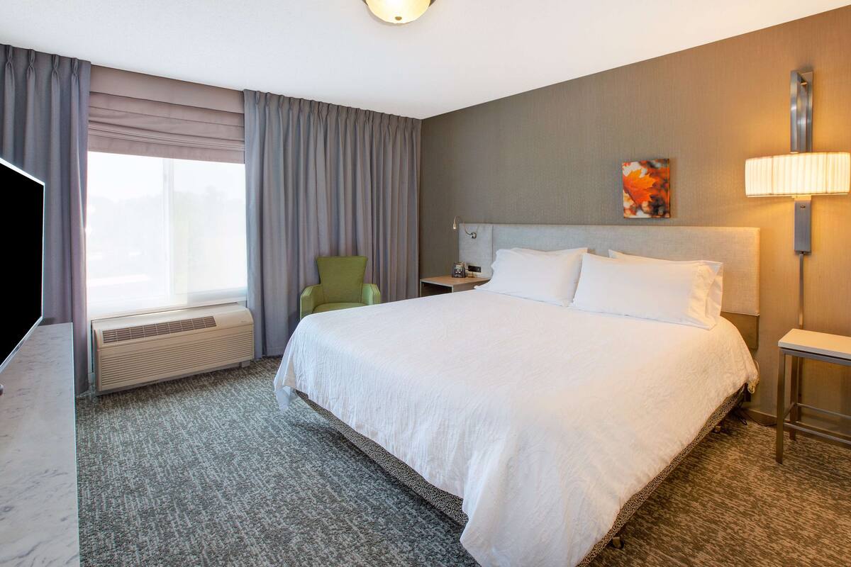 A hotel room with a large bed, a flat-screen TV, a desk, and a chair.