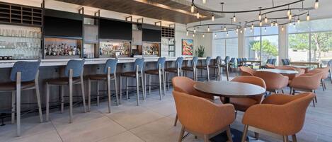Un área de bar moderna con varias opciones de asientos, incluyendo taburetes y mesas redondas con sillas.
