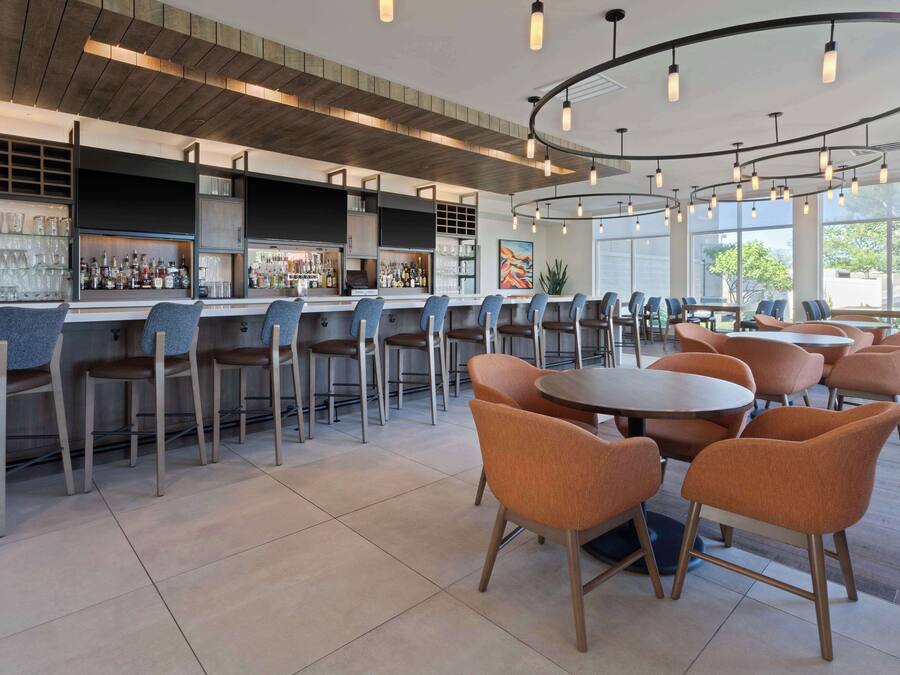 A modern bar area with multiple seating options, including bar stools and round tables with chairs.