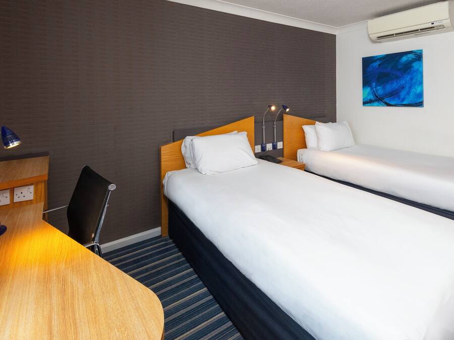 A hotel room with two beds, a desk, a chair, and an air conditioning unit.