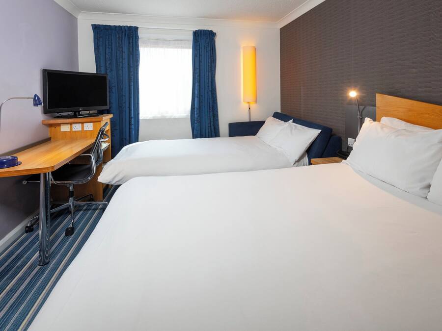 Une chambre d’hôtel avec deux lits, un bureau avec un ordinateur, une télévision et une lampe.
