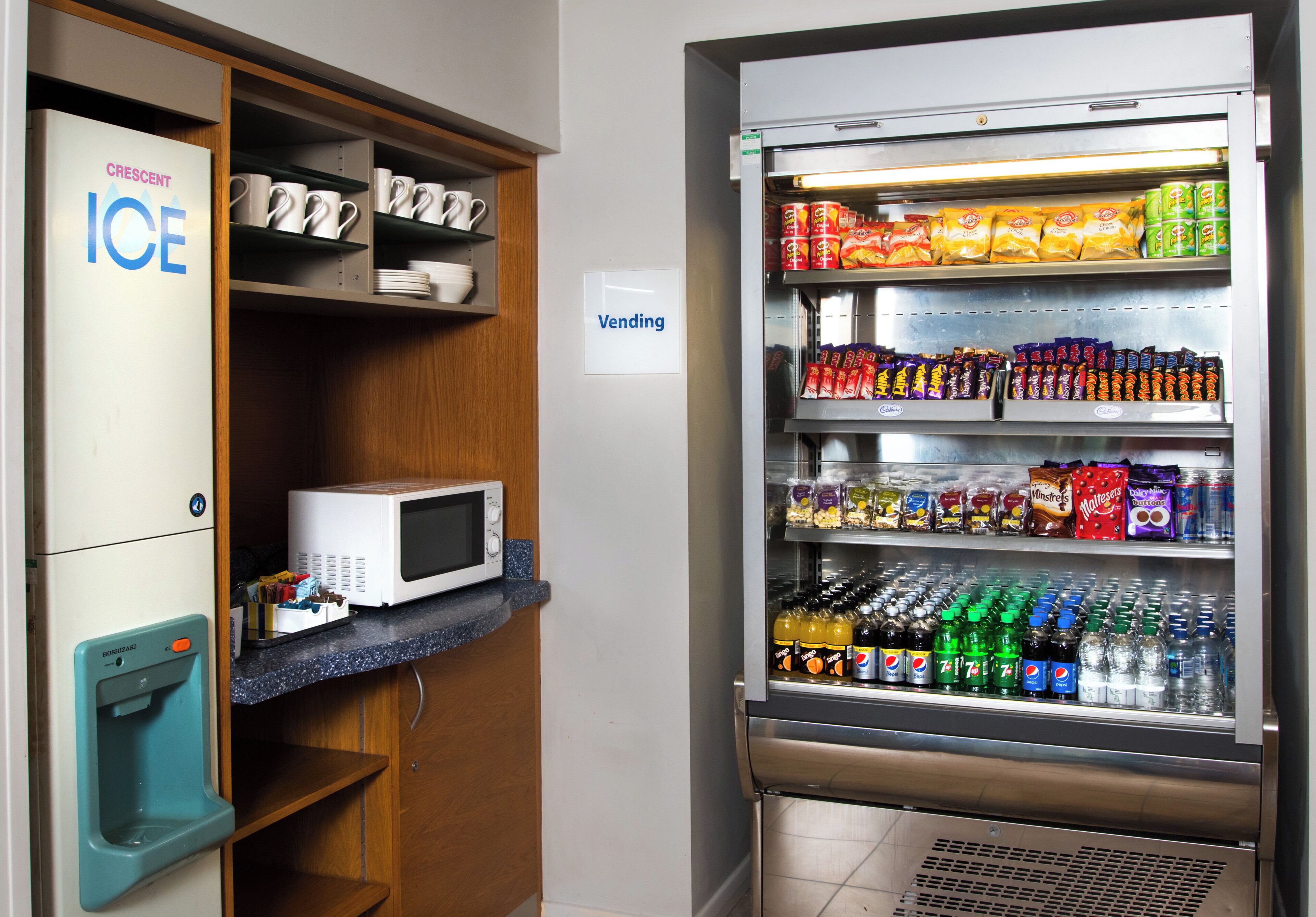 A vending machine stocked with snacks and beverages, a microwave, and a refrigerator with a 'Vending' sign.