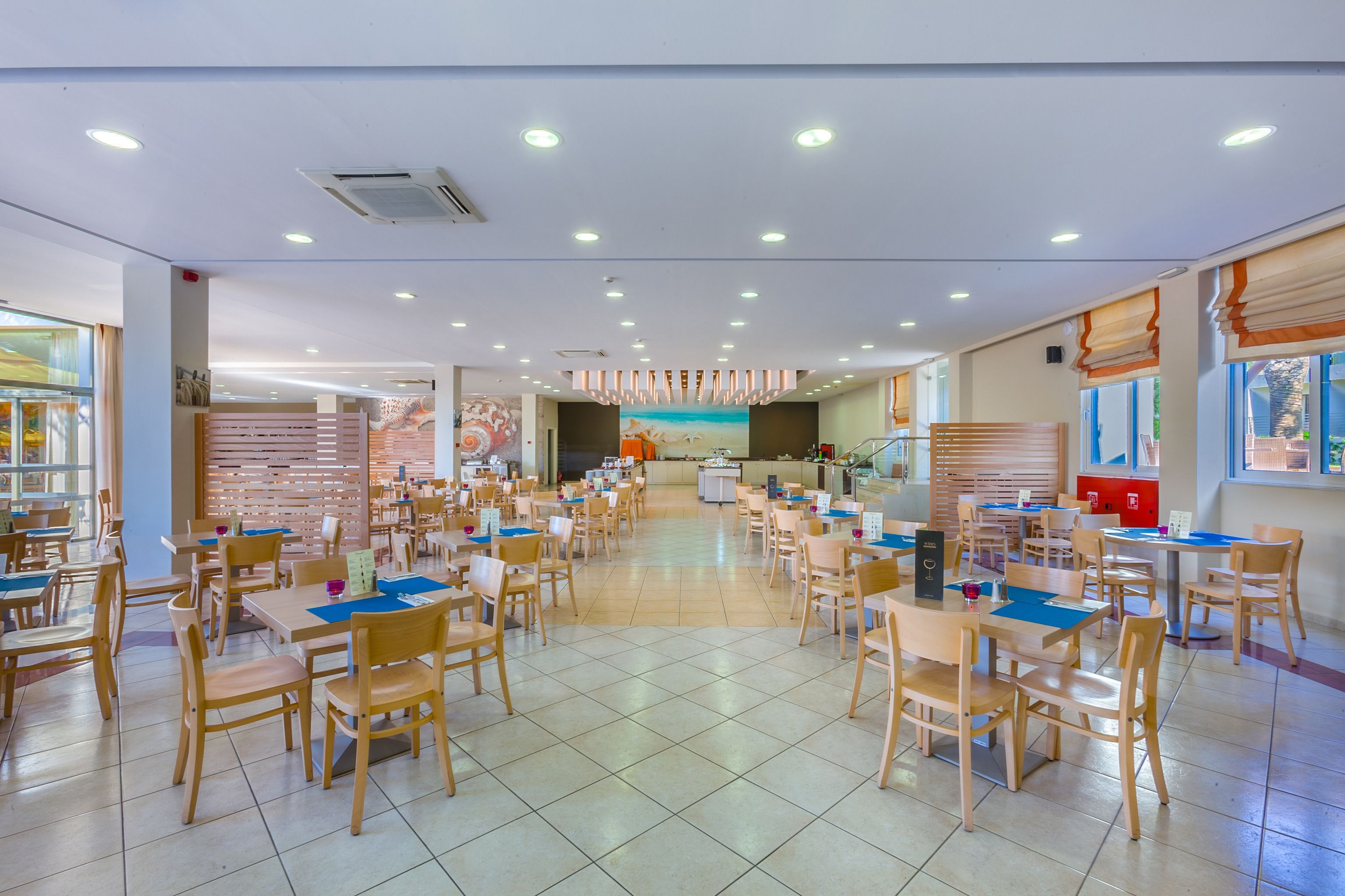 A spacious dining area with multiple tables and chairs, a central counter, and a mural on the back wall.