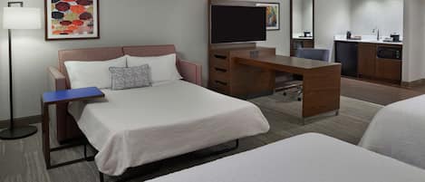 Habitación de hotel con cama, escritorio, silla y una pequeña kitchenette.