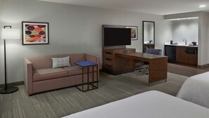 A hotel room with a bed, a desk with a computer, a sofa, a small table, a lamp, a TV, a kitchen area, and a bathroom. - Hampton Inn & Suites by Hilton Montreal-Dorval (Dorval)