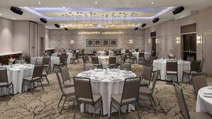 A spacious banquet hall with round tables, chairs, and a modern chandelier. - Hampton Inn & Suites by Hilton Montreal-Dorval (Dorval)