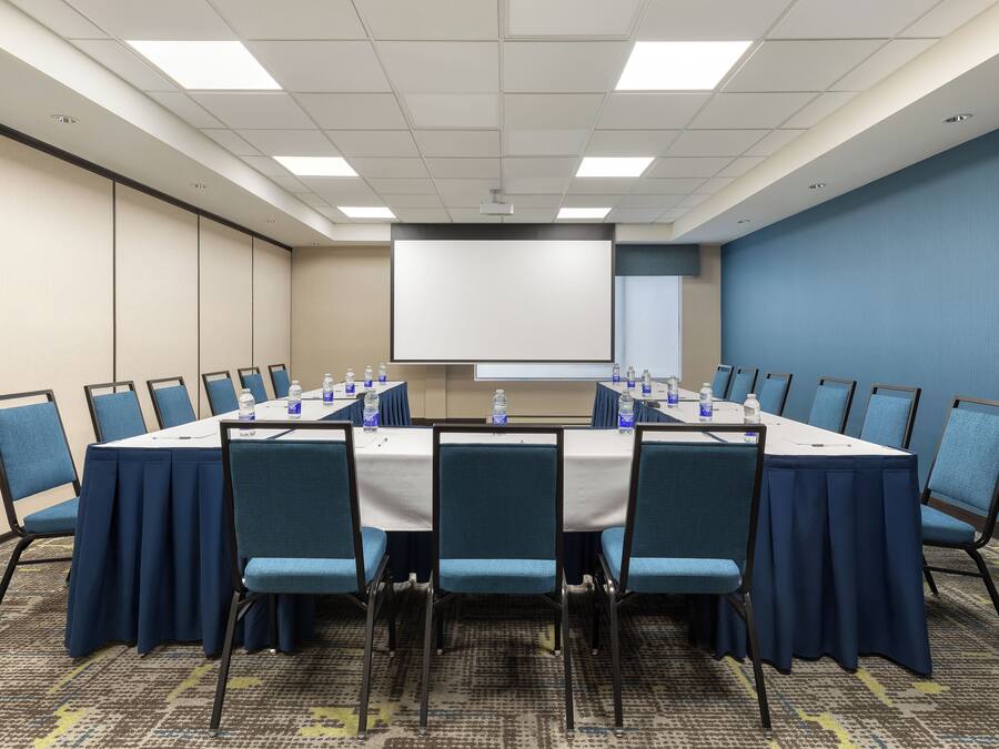 Un salón de conferencias con una larga mesa, sillas azules y una pantalla para proyector.