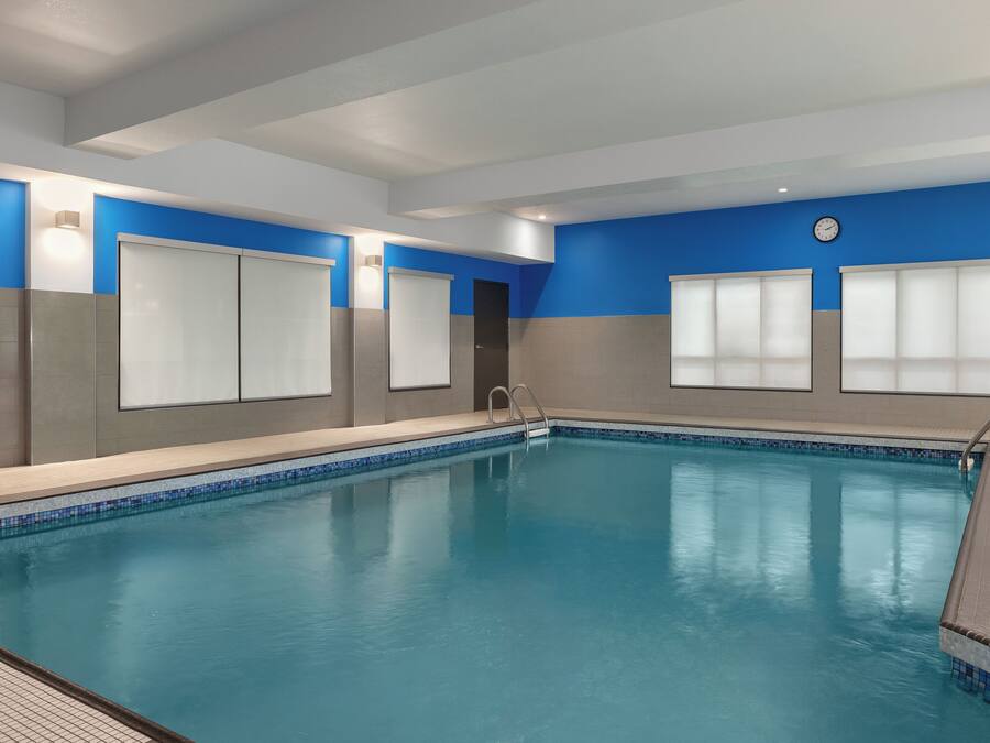 Une piscine intérieure à l’eau d’un bleu limpide, entourée de murs ornés de panneaux bleus et gris, et une horloge fixée au mur.