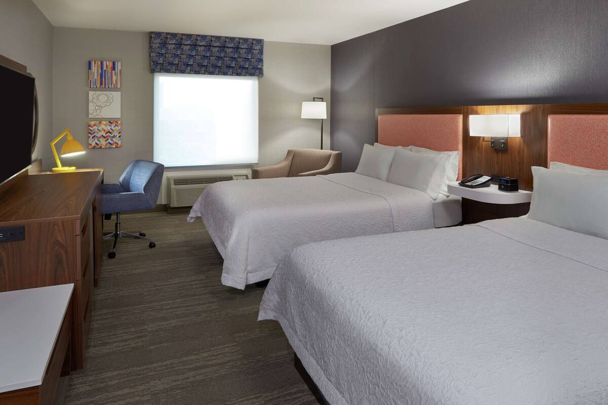Une chambre d’hôtel avec deux lits, un bureau, une chaise, une télévision et une fenêtre donnant sur un paysage agréable.
