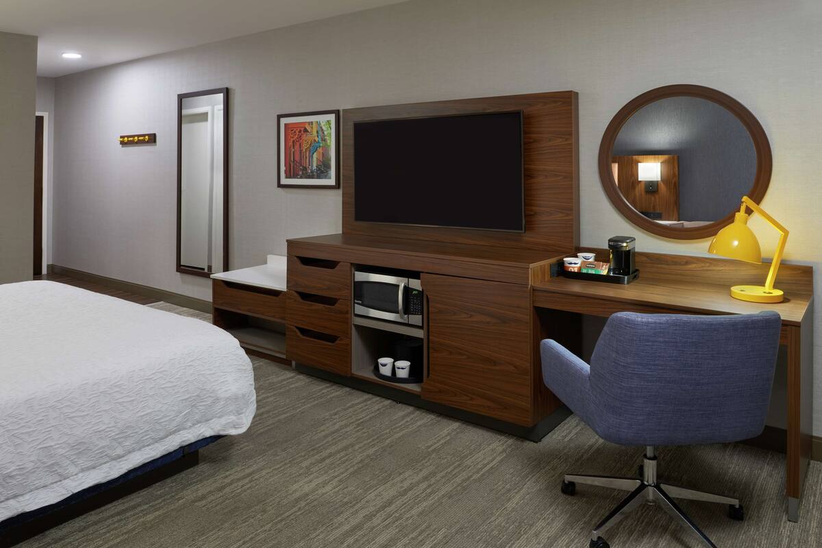 Une chambre d’hôtel comprenant un lit, un bureau avec un téléviseur à écran plat, un miroir, une lampe de bureau et une chaise.