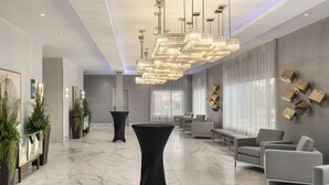 A modern lobby with marble flooring, a central black table, grey sofas, and a large chandelier. - Hampton Inn & Suites by Hilton Montreal-Dorval (Dorval)