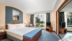 Habitación de hotel con una cama grande, televisión, escritorio con lámpara y vistas al exterior.