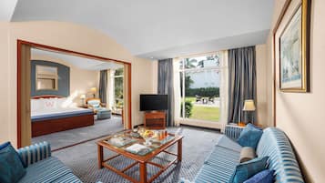 Habitación de hotel con cama, sofá, mesa de centro, televisor y vistas al exterior.