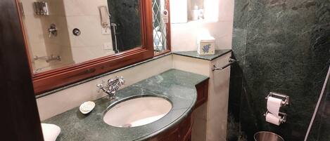 Un baño con lavamanos de mármol, un espejo, inodoro y un cubo de basura.
