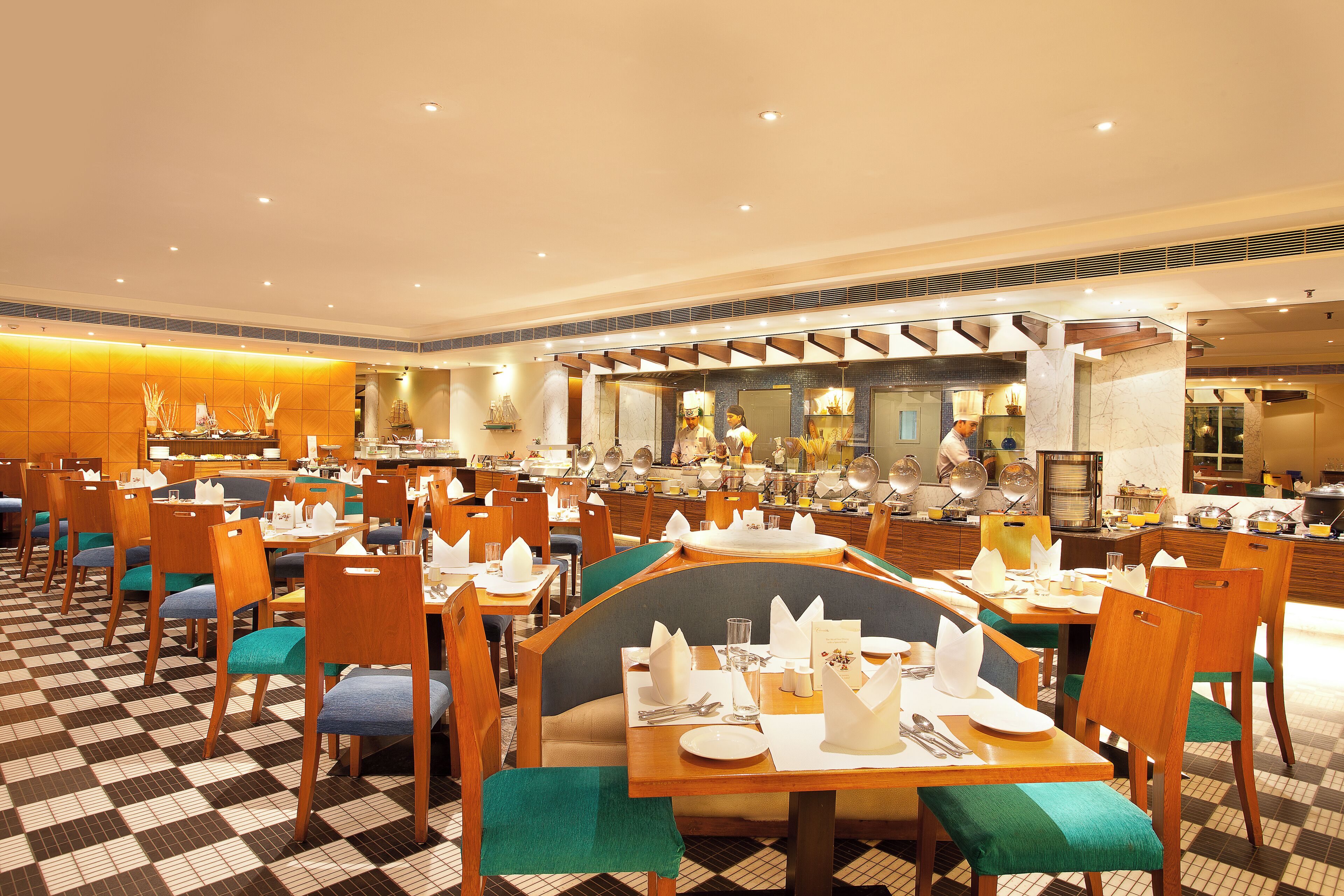 Un comedor de hotel con varias mesas y sillas, un suelo a cuadros y un mostrador de buffet al fondo.