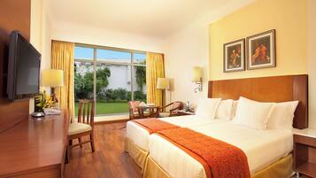 A hotel room with a large bed, two bedside tables, a desk with a chair, a TV, and a window with curtains.
