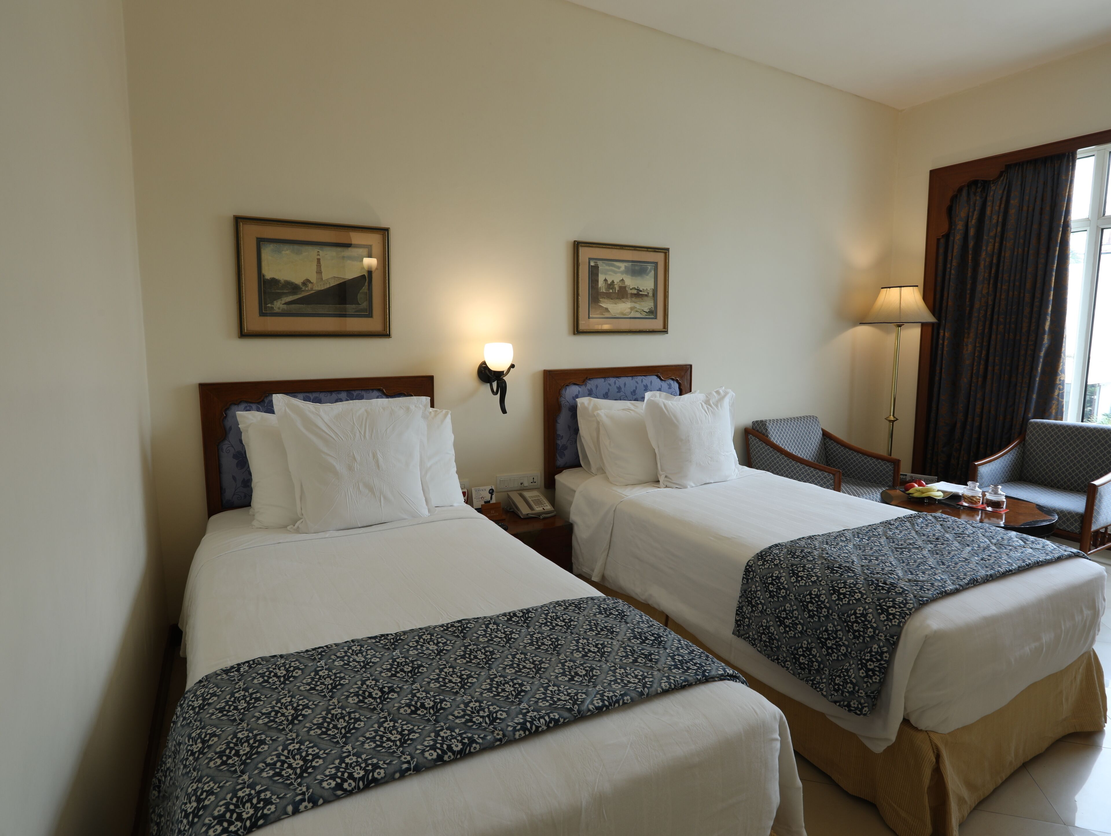 Habitación de hotel con dos camas, un escritorio, una silla y dos lámparas fijadas a la pared.
