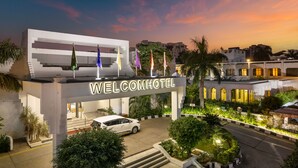 Entrada del Welcom Hotel con diseño moderno, un automóvil estacionado frente a ella y un camino bien iluminado que lleva a la entrada.