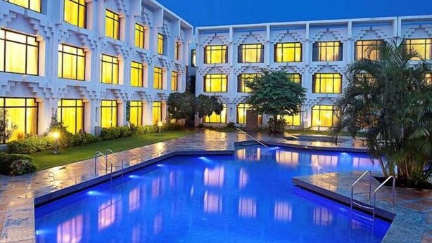 Un hotel con piscina, varios balcones y un patio con palmeras.