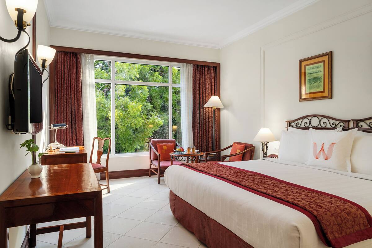 Habitació d'hotel amb un llit gran, una escriptori, una cadira, una taula amb una làmpada i una televisió.