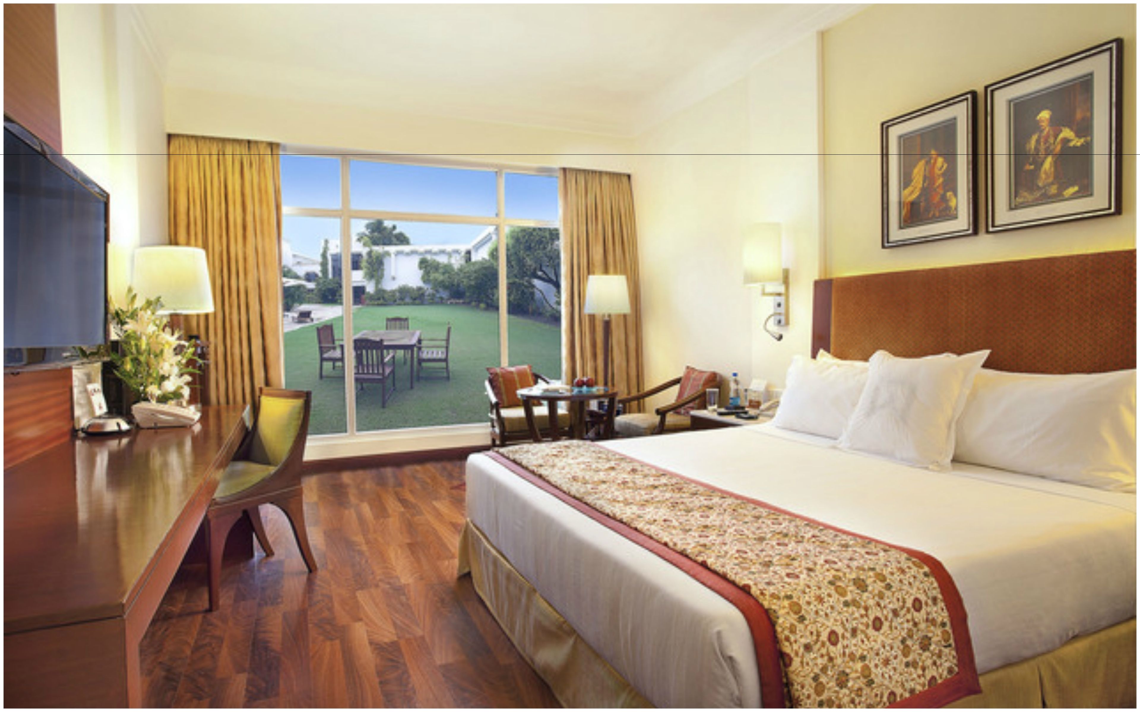 A hotel room with a large bed, a desk, a chair, a small table, and a view of the outdoors.