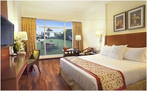 Une chambre d’hôtel avec un grand lit, un bureau, une chaise, une petite table et une vue sur l’extérieur.