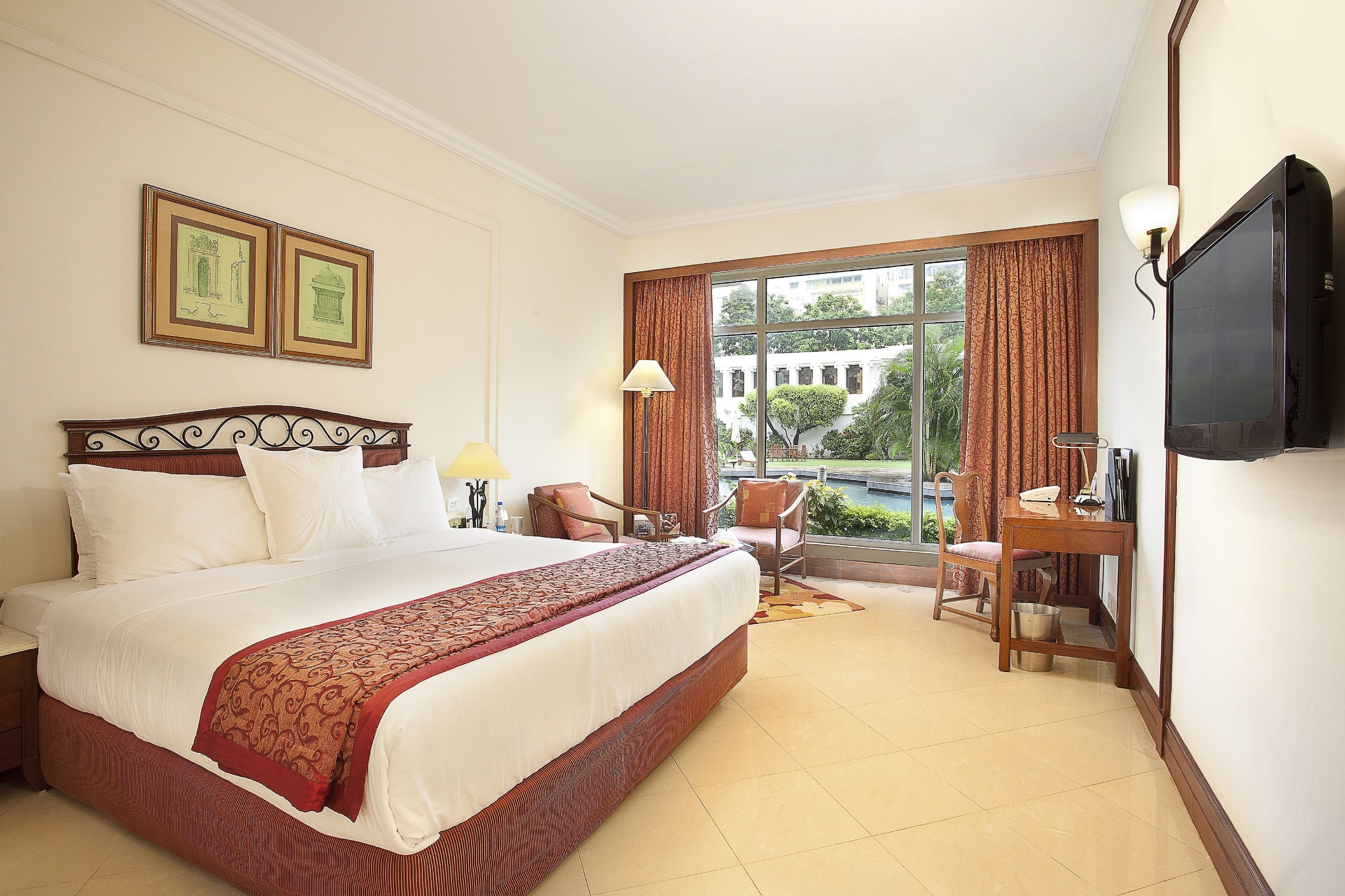 A hotel room with a large bed, two chairs, a desk, a television, and a window with curtains.