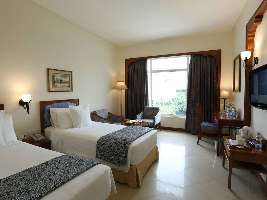 A hotel room with two beds, a desk, a chair, a TV, and a window with curtains.