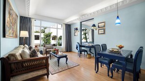 Amplia sala de estar con sofá, mesa de centro, mesa de comedor y sillas. Cuenta con un ventanal con cortinas, un cuadro en la pared y una lámpara colgante.