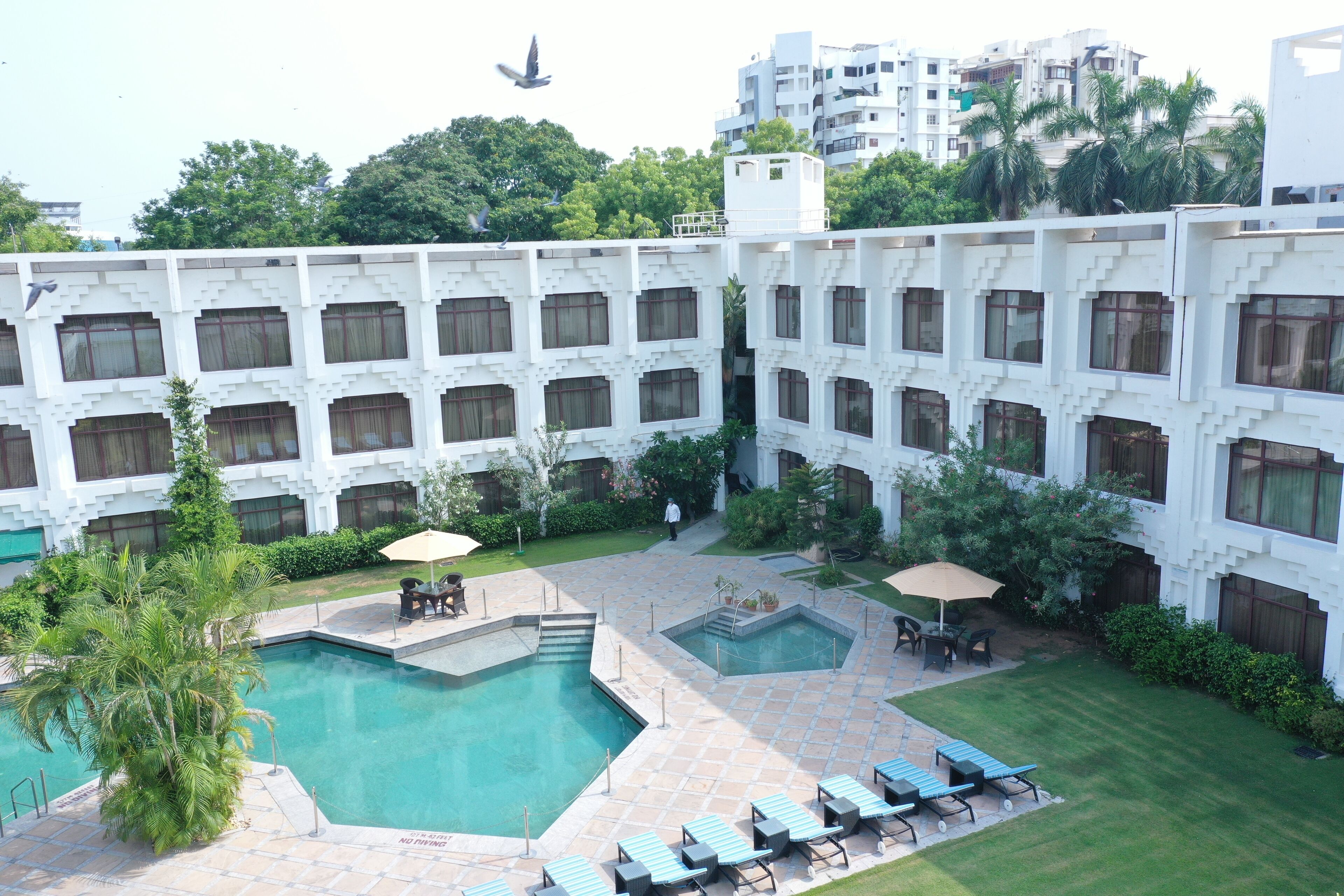 Une cour d’hôtel dotée de plusieurs piscines, de chaises longues et d’un espace de détente central.