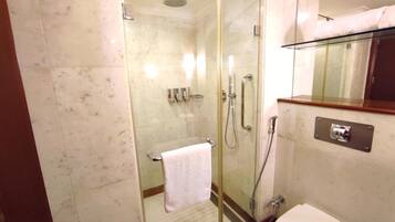 A glass-enclosed shower area with a white toilet and a towel rack.