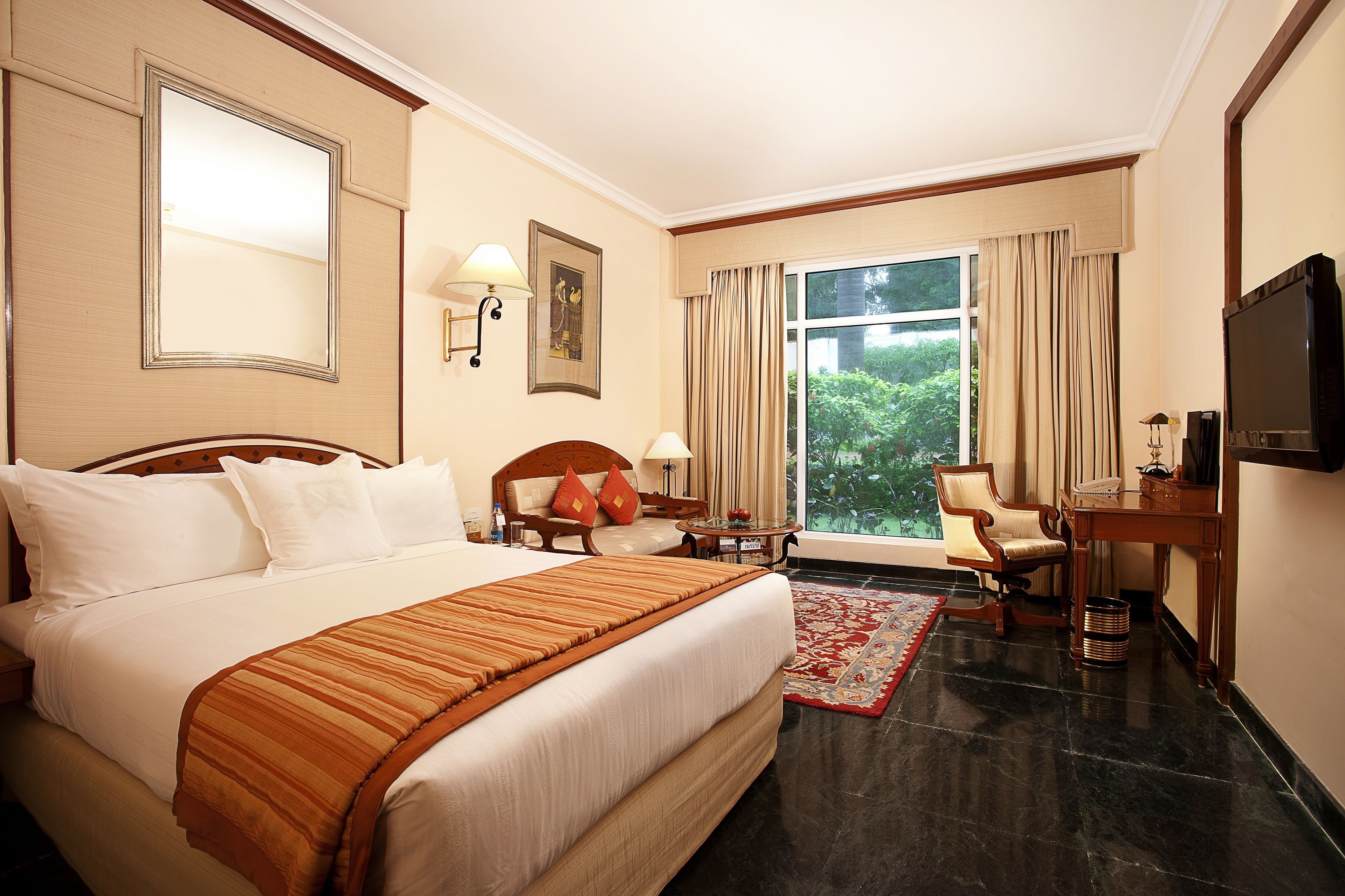 A hotel room with a large bed, a desk, a chair, a TV, and a window with curtains.