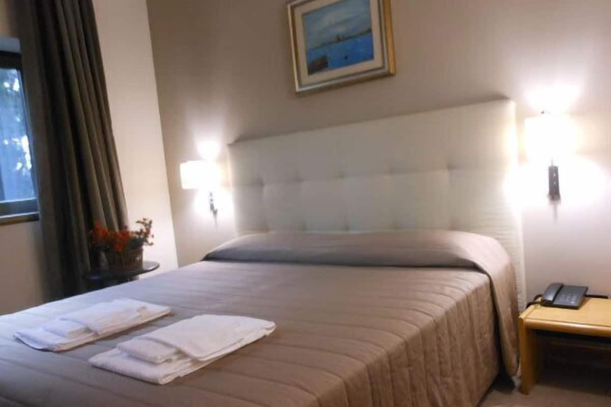 A neatly made bed with white towels, a headboard, bedside lamps, and a framed picture on the wall.