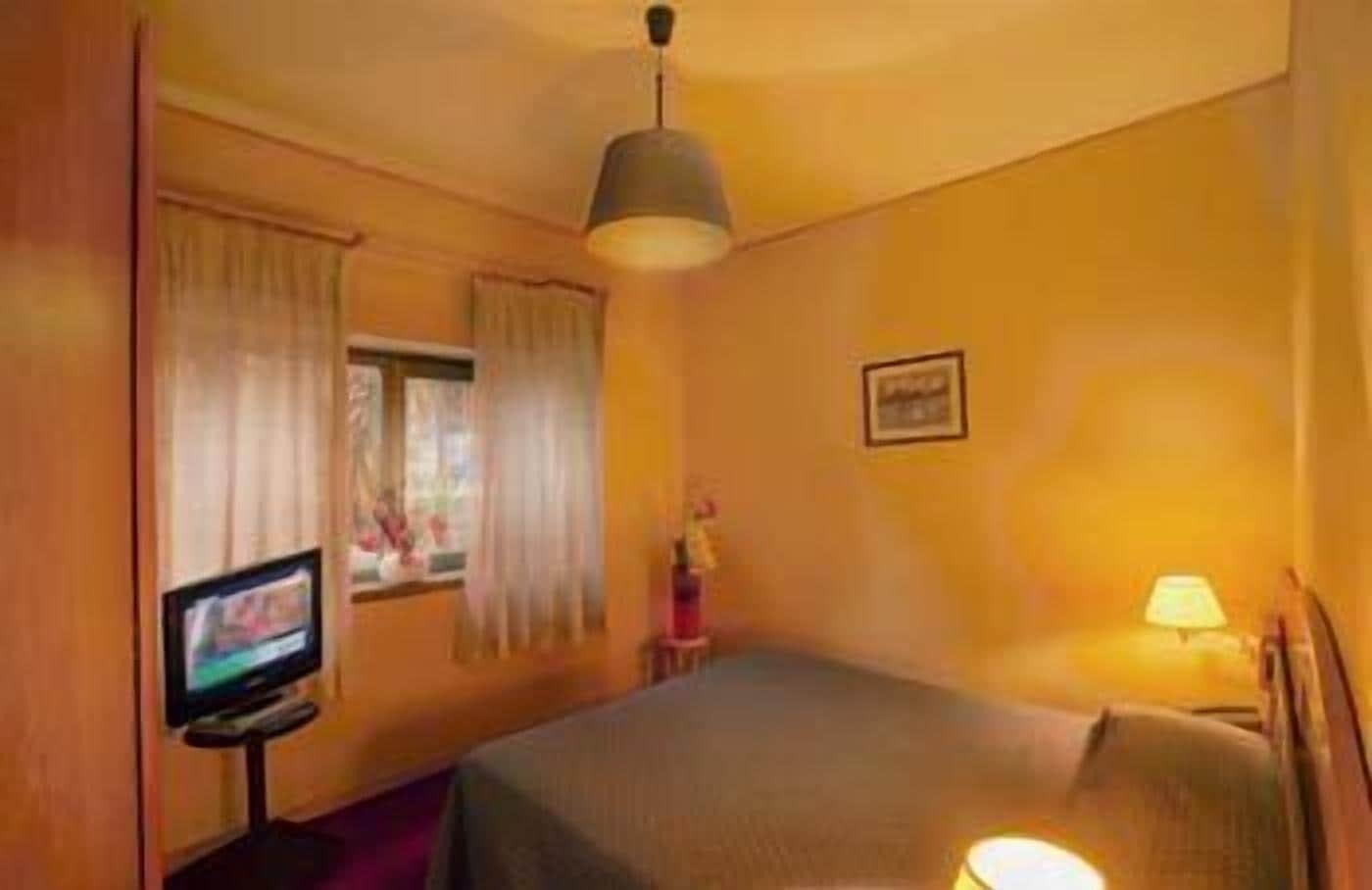 A hotel room with a bed, a television on a stand, a lamp, and a window with curtains.
