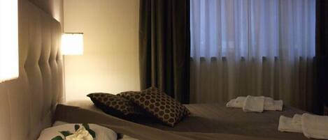 Una habitación de hotel con una cama, una mesita de noche, una lámpara y una ventana con cortinas.