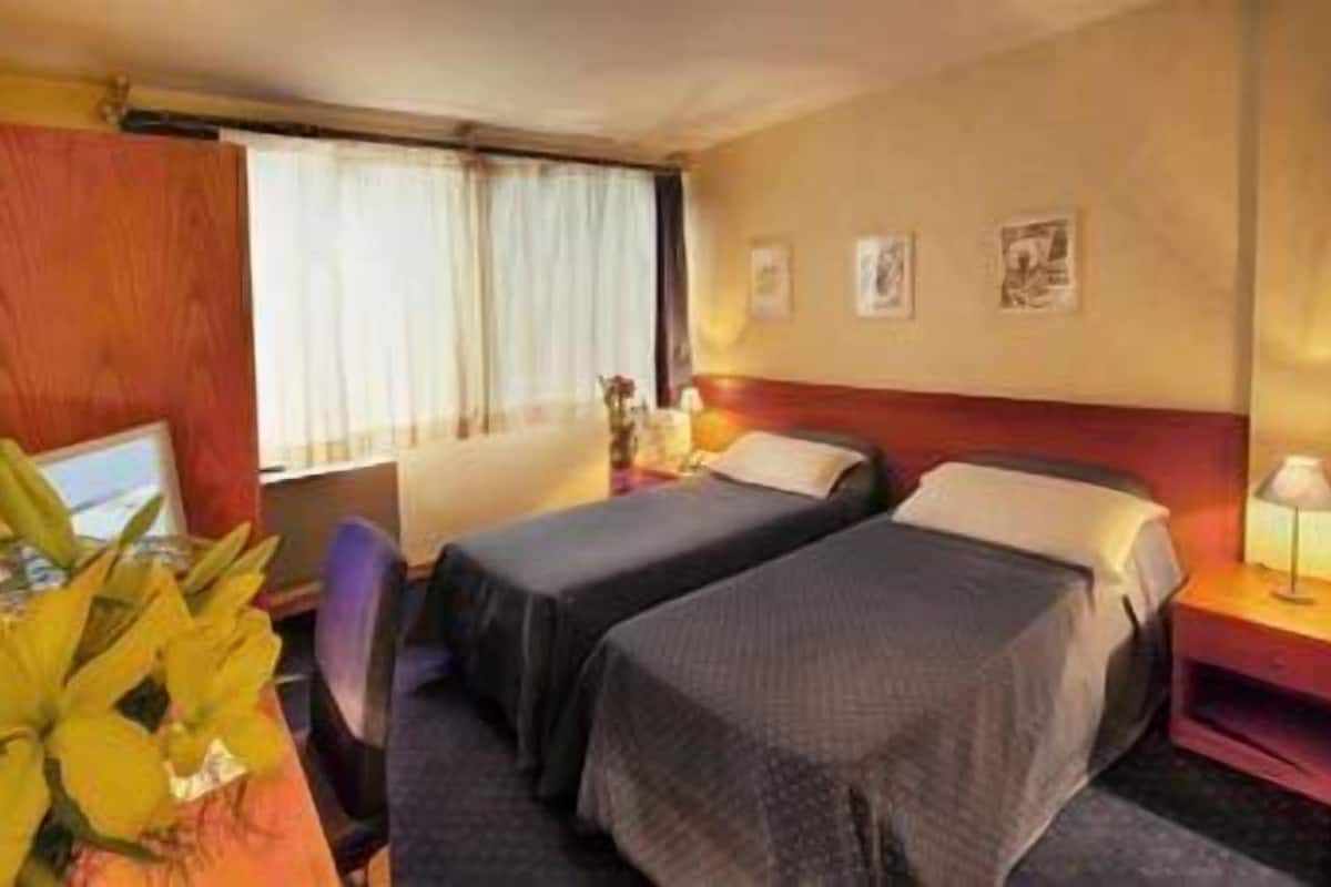 A hotel room with two beds, a desk with a computer, and a window with curtains.