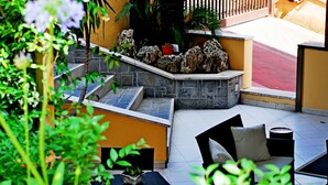 Zona de pati amb seients exteriors, mur de pedra i plantes en testos.