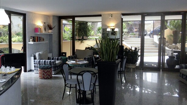 Un vestíbul d'hotel modern amb una zona de dinar, zones d'estar i una escala que condueix a una zona exterior.