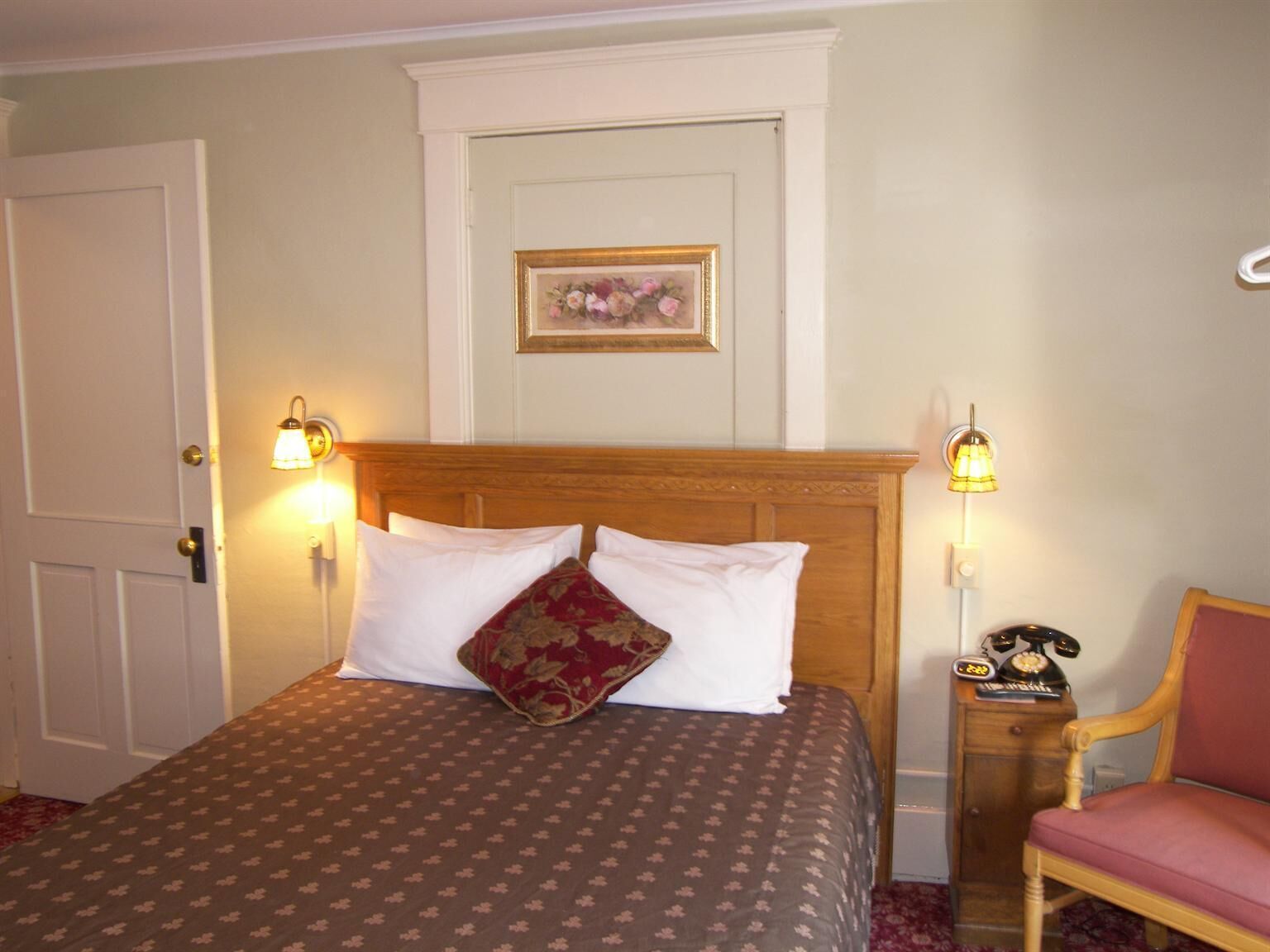Une chambre d’hôtel comprenant un lit, deux lampes de chevet, une tête de lit en bois, une table de chevet avec un téléphone et une chaise.