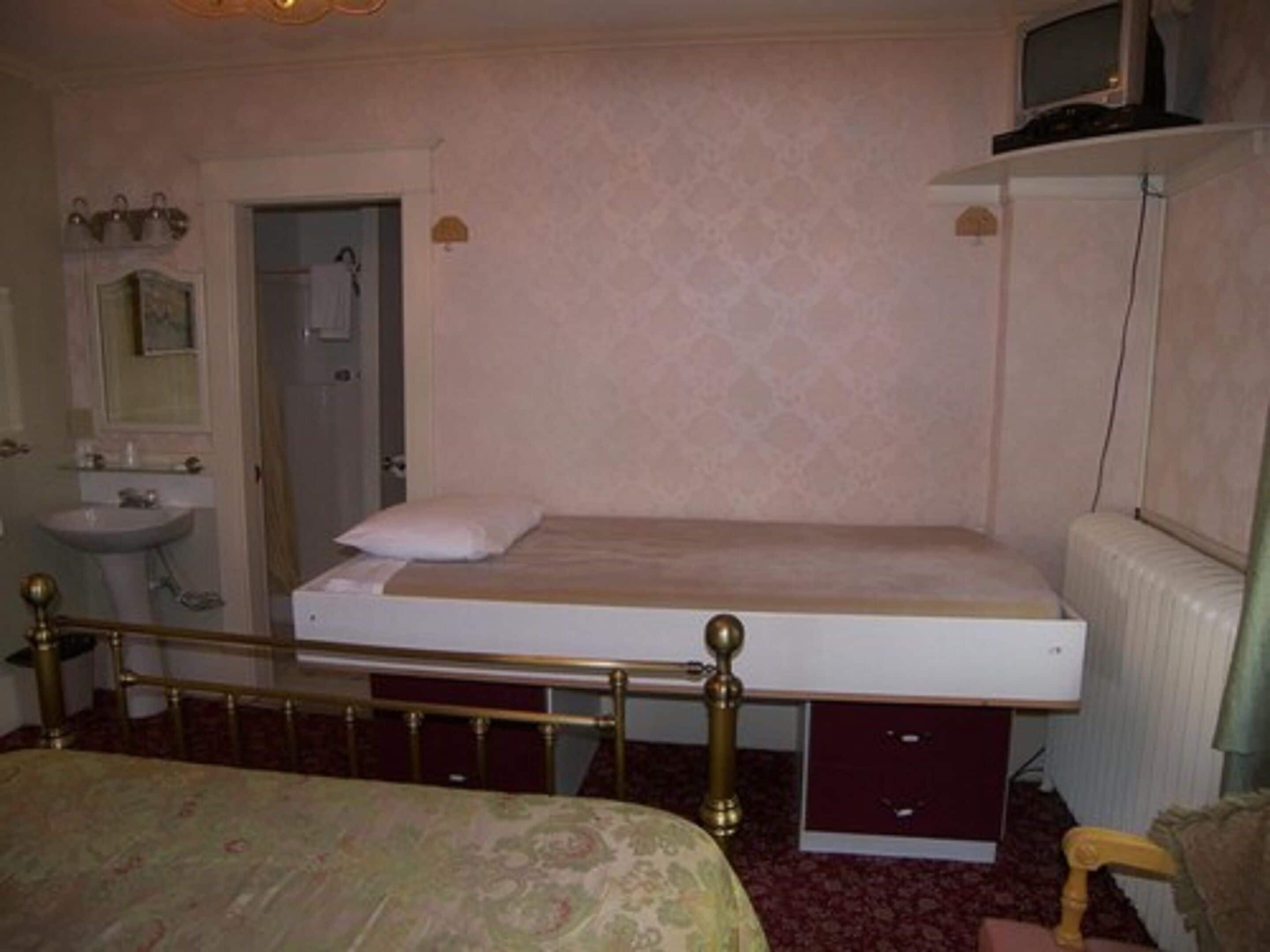 Un dormitorio con una cama individual, una mesita de noche, un espejo, un radiador y un televisor sobre una estantería.