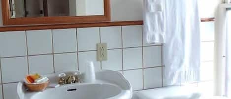 Um banheiro com pia de pedestal, vaso sanitário e bidê. Há um espelho sobre a pia e um quadro na parede.