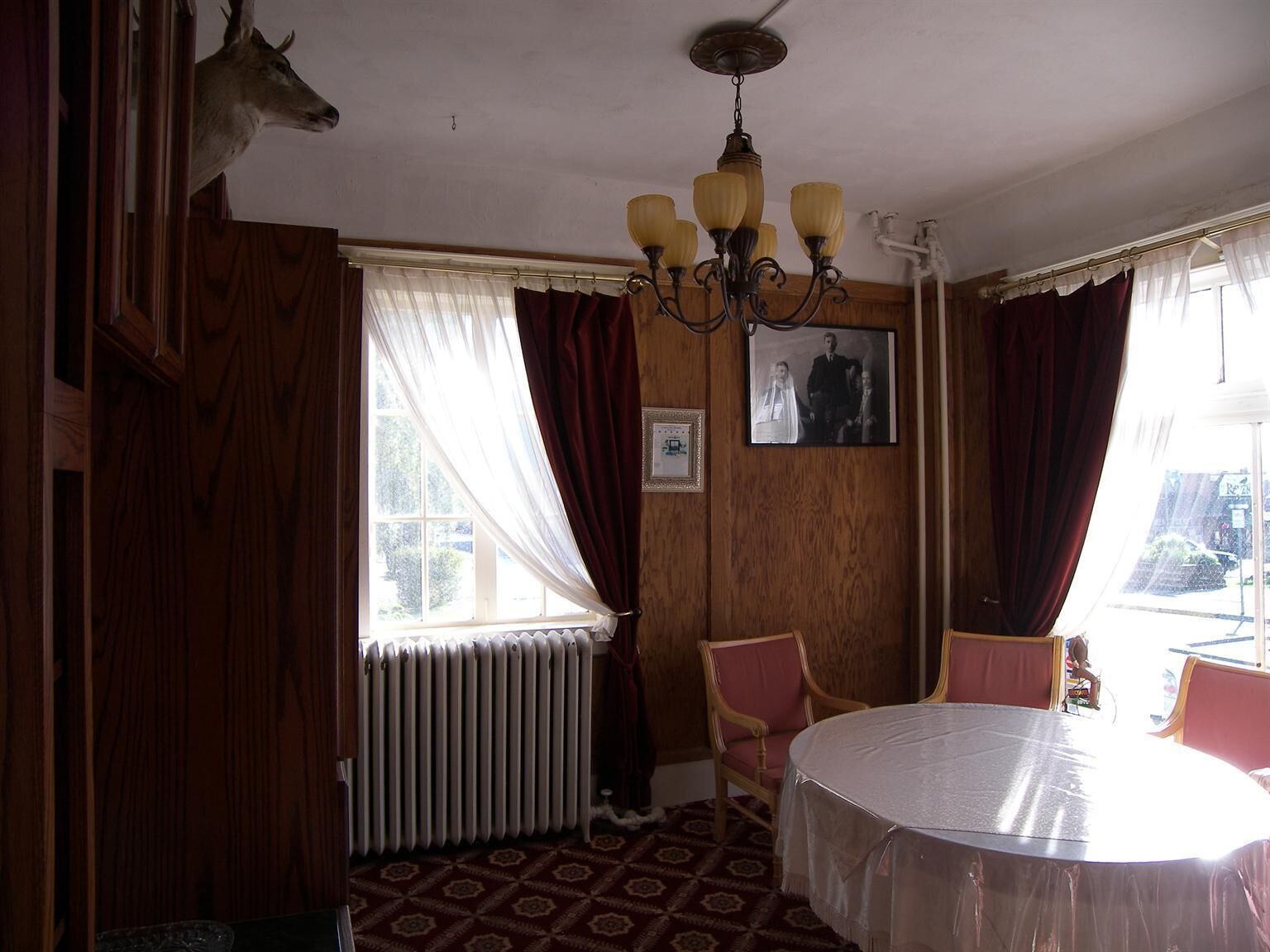 A dining room with a round table, chairs, a chandelier, a radiator, and a framed photo on the wall.