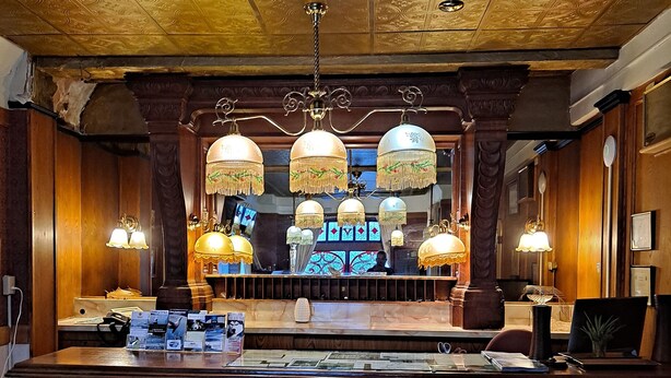 A bar area with a wooden counter, hanging lamps, and two stools. - Van Gilder Hotel (Seward)