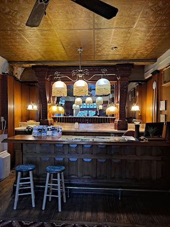 A bar area with a wooden counter, hanging lamps, and two stools.