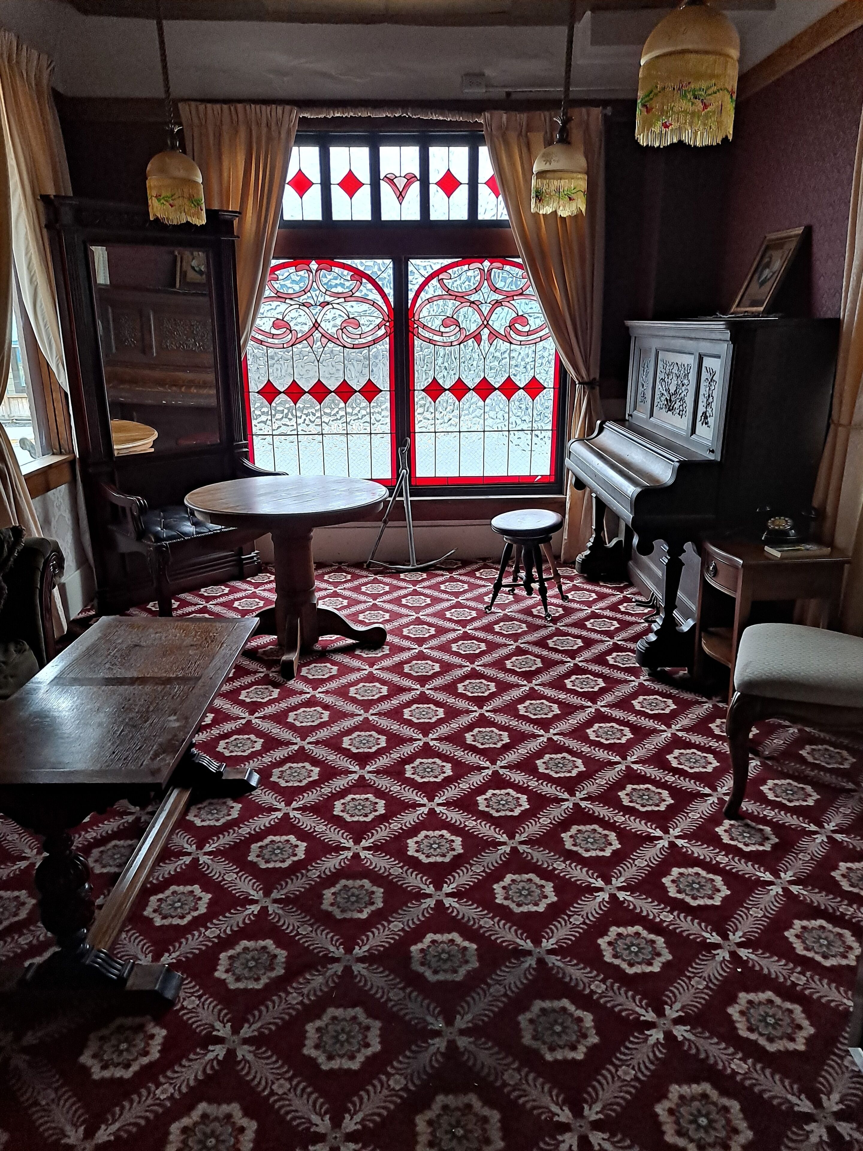 Una habitación con alfombra estampada, un piano, una mesa y una silla.