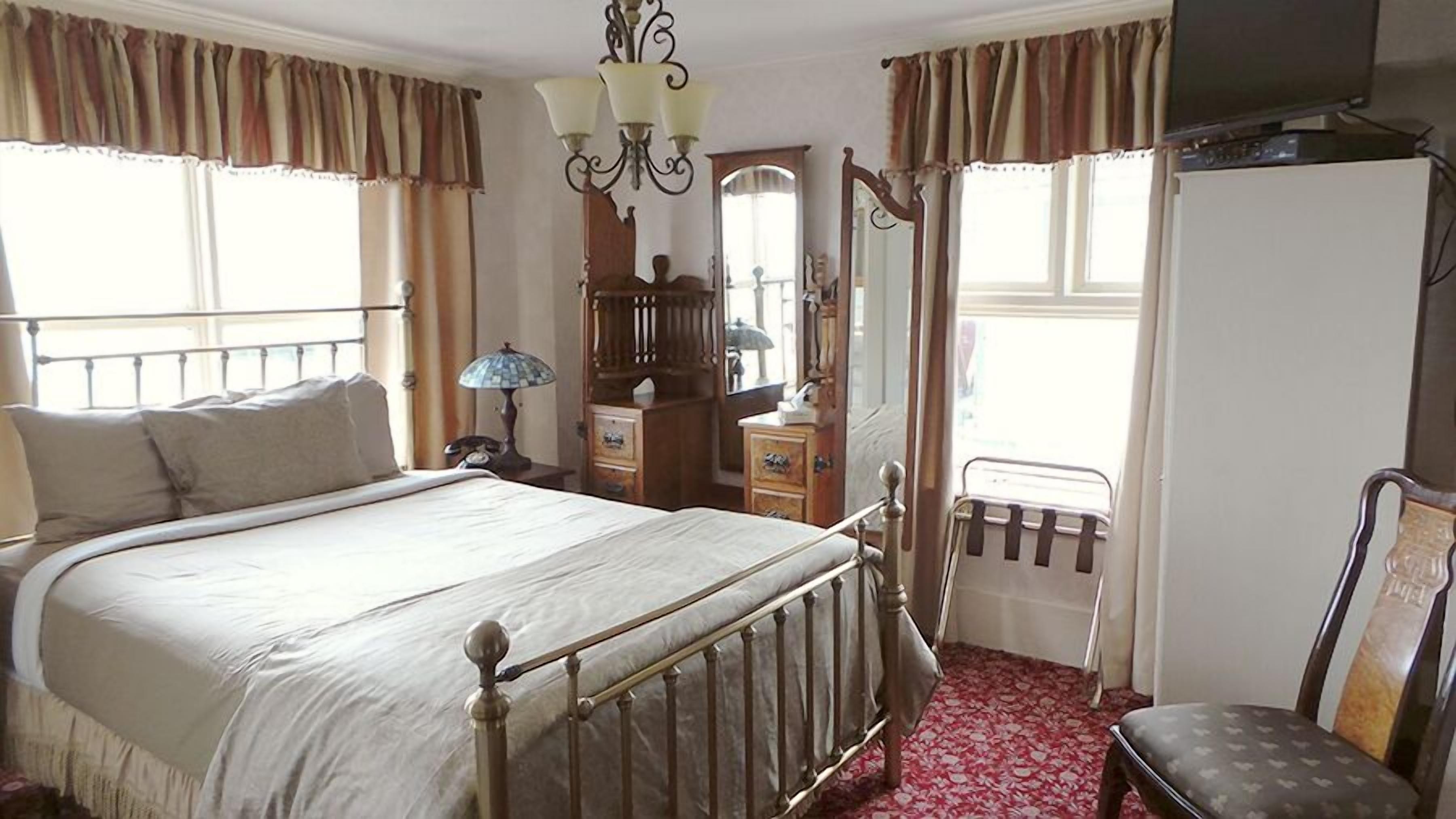 Un dormitorio con cama, cómoda, espejo, radiador y una silla.
