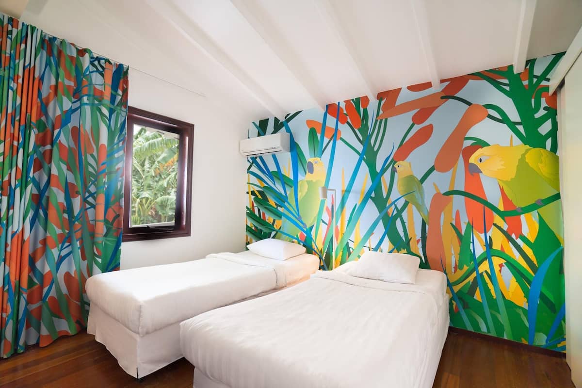 Una habitación con dos camas, una ventana y un mural de pared colorido.