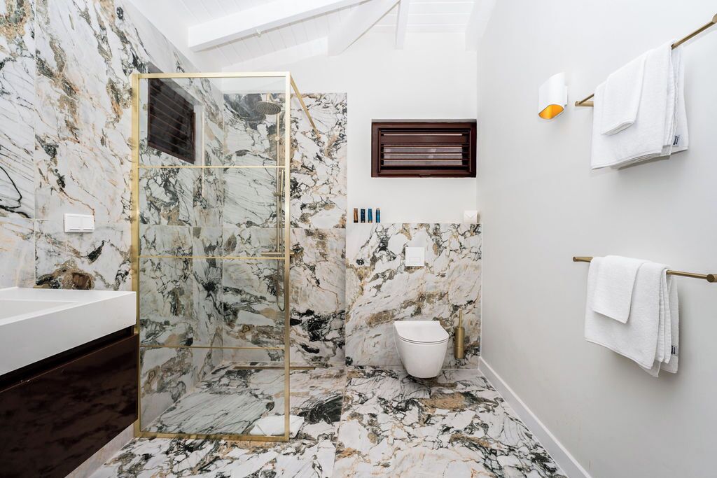 Un baño moderno con cabina de ducha de vidrio, suelo de mármol, lavamanos blanco y un perchero para toallas.