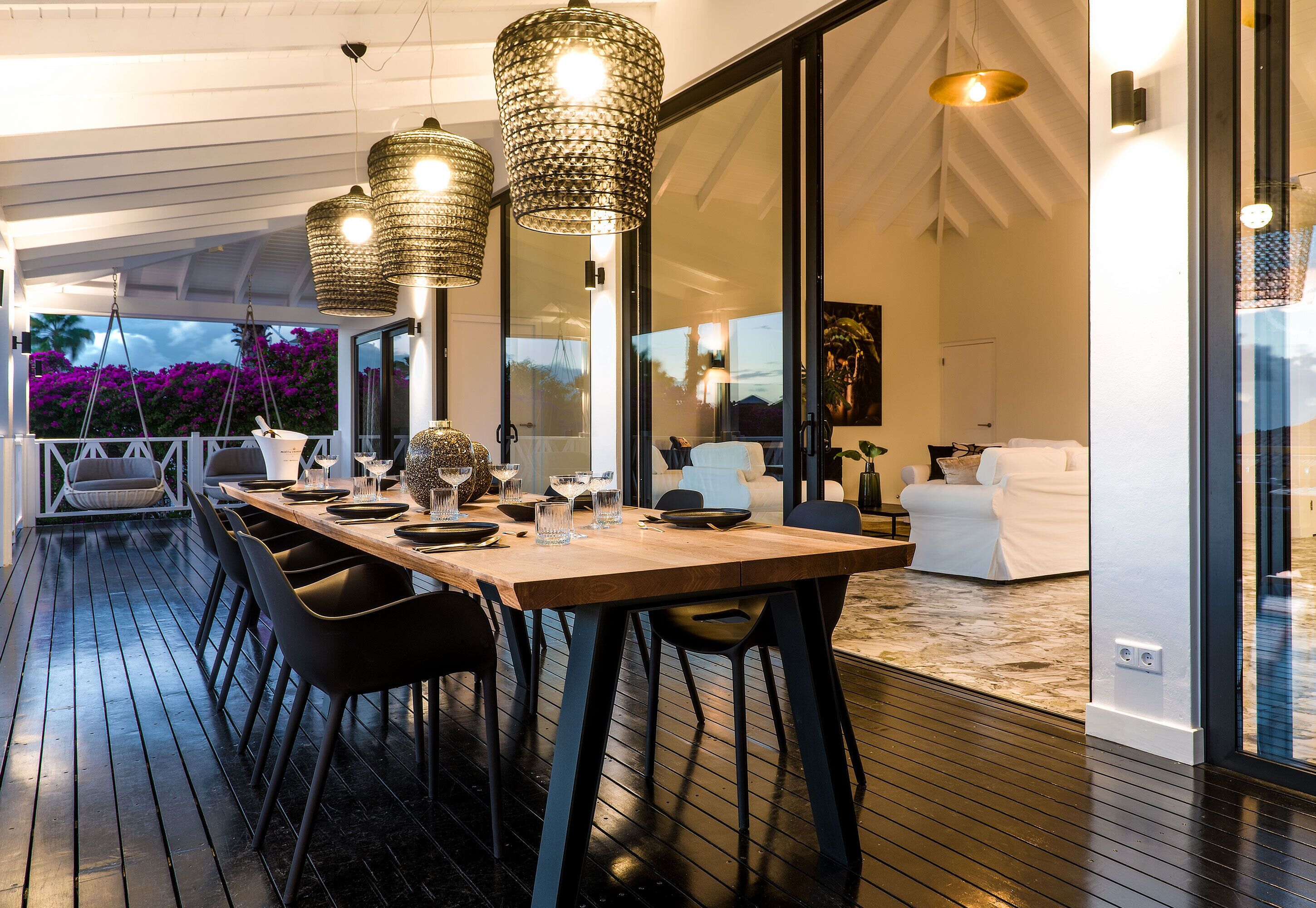 A dining area with a wooden table and black chairs, large hanging lights, and a view of the outdoors.